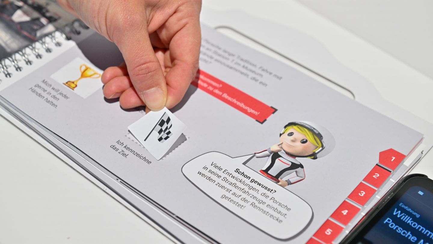 Die richtigen Antworten stickern die Kinder in ihr Mitmach-Buch, 2023, Porsche AG